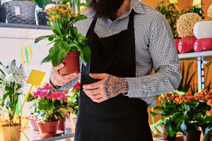 Homem de barba e avental segurando vaso com flores amarelas
